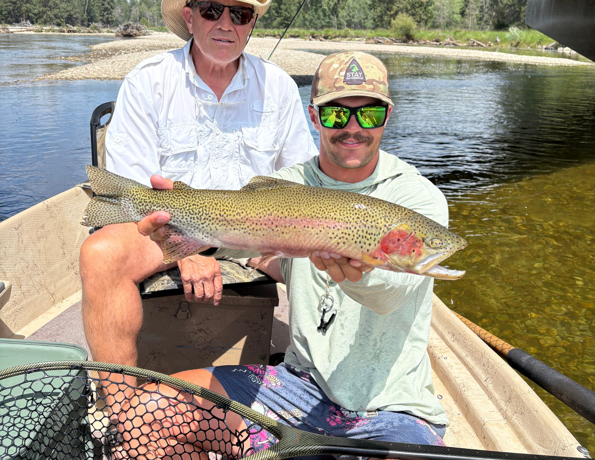 Two men in a boat holding a large rainbow trout by a the Bitterroot River